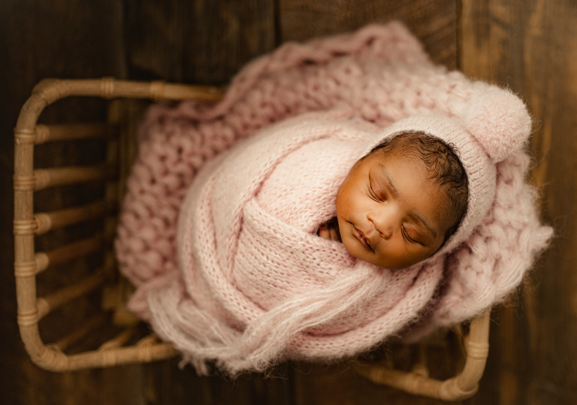 newborn baby in pink swaddled lying in baby bed prop
