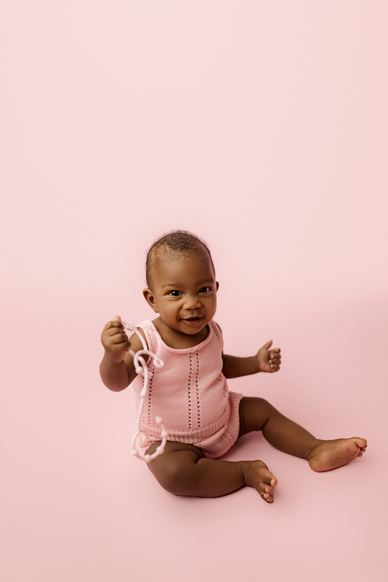 smiling baby sitting on pink backdrop